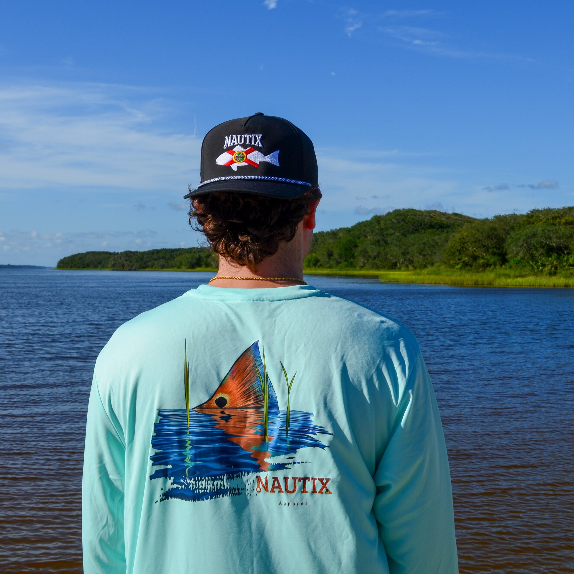 Model wearing blue performance tee with large Tailing Red redfish artwork on back
