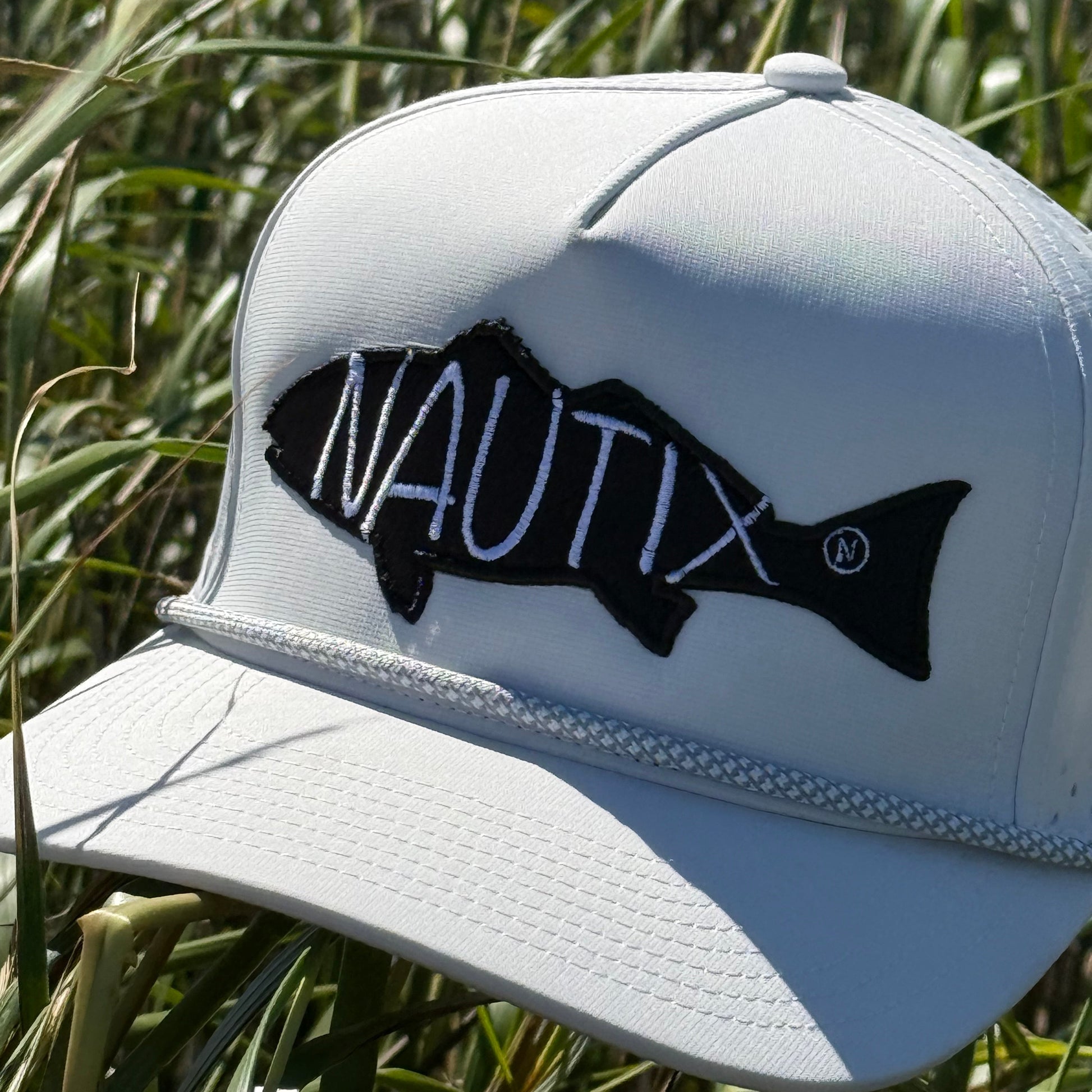 White Nautix hat with black fish logo in grass