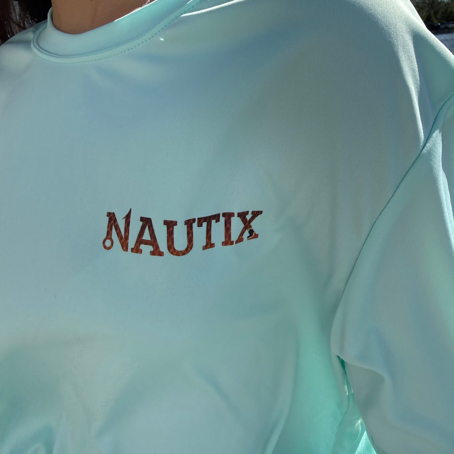 Close-up of Nautix logo with fish-scale pattern on blue performance shirt