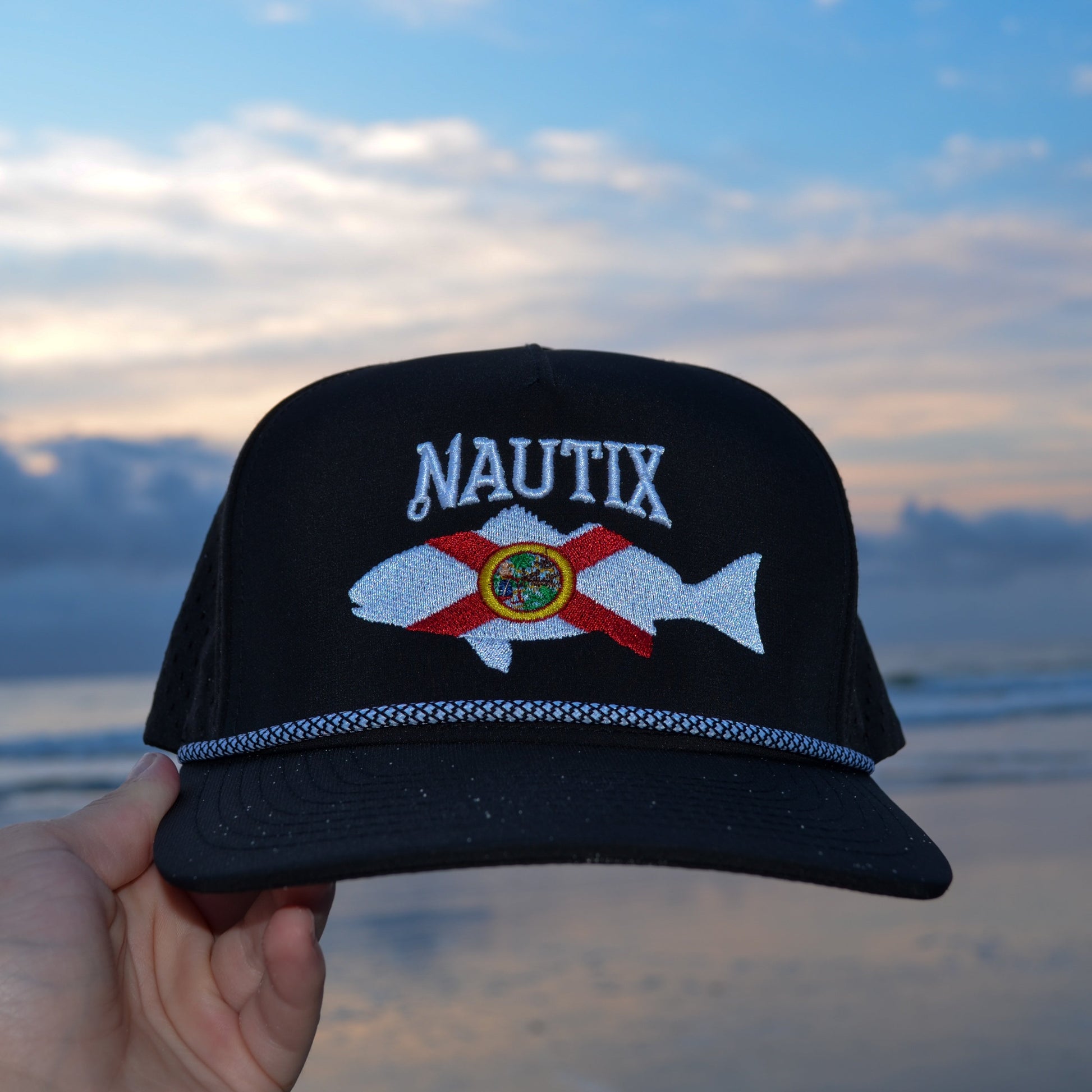 Close up of embroidered Nautix Florida logo on black hat at the beach